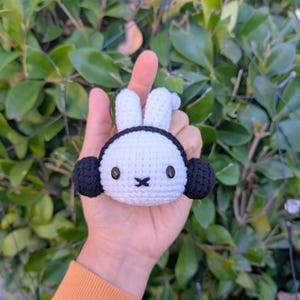 May include: A white crocheted bunny with black ears and black button eyes. The bunny is being held in a hand.