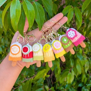 May include: Seven crochet popsicle keyrings in assorted colours and fruit designs. Each keyring has a gold-coloured clasp and chain. The popsicles feature orange, watermelon, lemon, and kiwi fruit designs, with brown popsicle sticks.