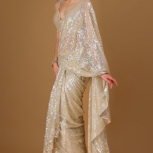 May include: A gold sequined saree with a draped design. The saree is made of a sheer fabric and has a shimmering finish.