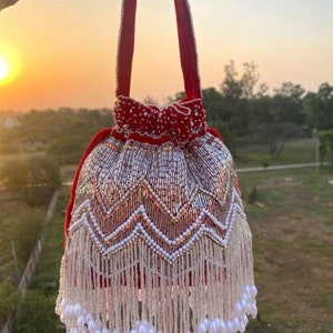 Peut inclure: Un sac à cordon en velours rouge avec des embellissements en perles argentées et blanches et une frange de perles blanches.