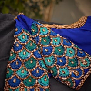 May include: A blue blouse with a peacock design embroidered on the sleeves. The embroidery features gold, blue, and green beads.
