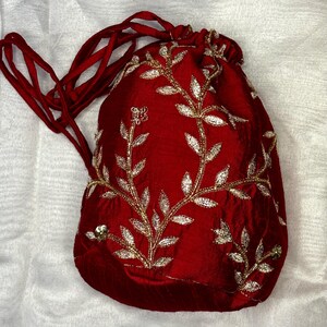 May include: A red velvet drawstring bag with gold leaf embroidery of a floral design. The bag has a long red drawstring.