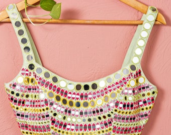 May include: A light green sleeveless blouse with a scoop neck and a decorative design of mirrored circles in shades of pink, yellow, and green.