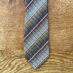 Może przedstawiać: Krawat w paski w kolorze brązowym, szarym i białym. Krawat wykonany jest z tkaniny tkanej i ma subtelny połysk.