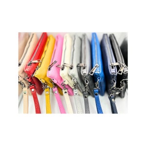 May include: A row of colorful leather zippered pouches with wrist straps. The pouches are in shades of red, yellow, pink, cream, gray, blue, and black.
