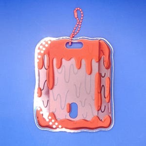 May include: A clear, rectangular ID badge holder with a red, drippy design. The holder has a small hole at the top and a red chain. The background is a solid blue.