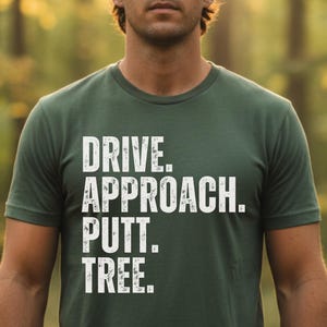 Könnte beinhalten: Dunkelgrünes T-Shirt mit dem weißen Schriftzug "DRIVE. APPROACH. PUTT. TREE." in Blockbuchstaben. Das kurzärmelige Shirt scheint aus einem weichen Material zu sein. Der Hintergrund ist eine verschwommene Waldszene.