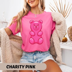 Puede incluir: Camiseta rosa con un dise&ntilde;o de osito de goma. La camiseta es de color rosa brillante, con el texto "CHARITY PINK" en la parte inferior. El osito de goma es de color rosa brillante.
