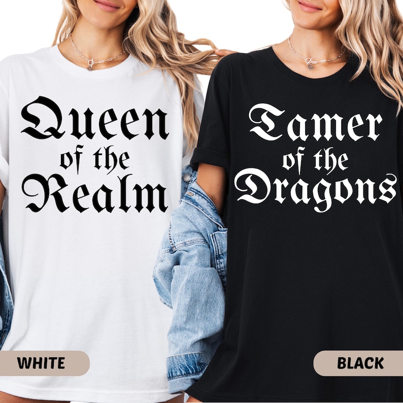 May include: Two t-shirts, one white and one black, with fantasy-themed text. The white shirt reads "Queen of the Realm" in a gothic font. The black shirt says "Tamer of the Dragons" in a similar style. The word "WHITE" is printed on the bottom of the white shirt, and "BLACK" on the black shirt.