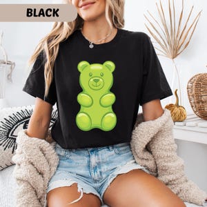 Puede incluir: Camiseta negra con un gran dise&ntilde;o de osito de goma verde. El texto "BLACK" se muestra en la parte superior de la imagen. Esta camiseta informal es adecuada para el uso diario. El estilo es c&oacute;modo.
