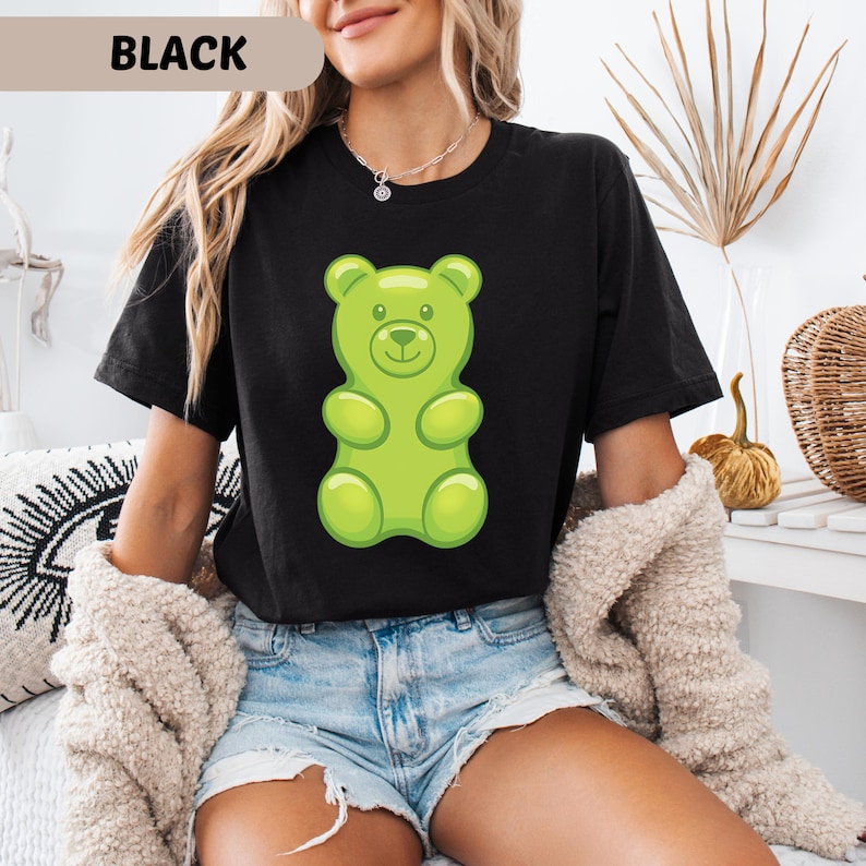 Puede incluir: Camiseta negra con un gran dise&ntilde;o de osito de goma verde. El texto "BLACK" se muestra en la parte superior de la imagen. Esta camiseta informal es adecuada para el uso diario. El estilo es c&oacute;modo.