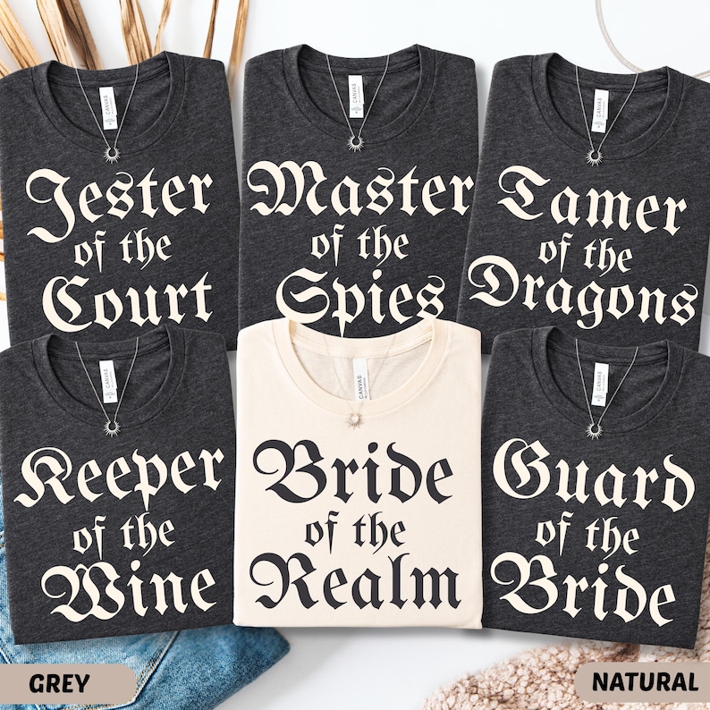 May include: A collection of t-shirts in grey and natural colors, each with a unique title in a gothic font. Titles include "Jester of the Court", "Master of the Spies", "Tamer of the Dragons", "Keeper of the Wine", "Bride of the Realm", and "Guard of the Bride".