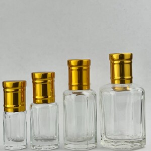 Puede incluir: Cuatro frascos de perfume de vidrio transparente con tapas doradas. Los frascos son de diferentes tama&ntilde;os, desde formas peque&ntilde;as y rectangulares hasta un dise&ntilde;o m&aacute;s grande y cuadrado. Las tapas tienen una textura acanalada.