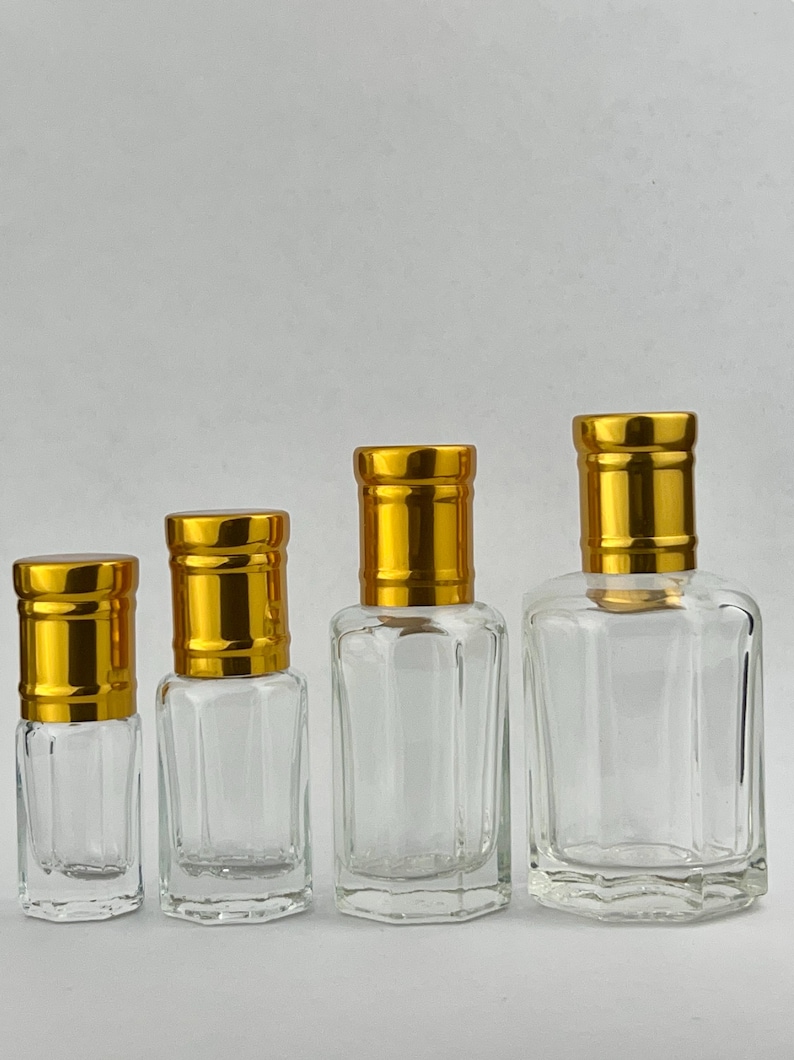 Puede incluir: Cuatro frascos de perfume de vidrio transparente con tapas doradas. Los frascos son de diferentes tama&ntilde;os, desde formas peque&ntilde;as y rectangulares hasta un dise&ntilde;o m&aacute;s grande y cuadrado. Las tapas tienen una textura acanalada.