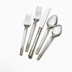 May include: A five-piece stainless steel flatware set including two forks, a dinner knife, a tablespoon, and a teaspoon. Each handle features a polished silver finish with decorative gold-toned bands and a textured, woven-look metal inlay.