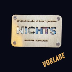 May include: A wooden sign with the text "Es war schwer, aber wir haben's gefunden: NICHTS Herzlichen Glückwunsch!" The sign is light brown with a dark brown border and silver screws in each corner. The word "NICHTS" is cut out of the sign and filled with a colorful pattern.