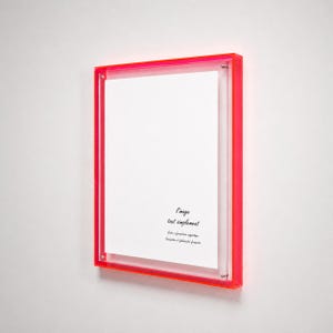 Peut inclure: Un cadre photo rectangulaire doté d'une bordure en acrylique rose néon vif. Le cadre contient un insert blanc avec le texte imprimé en noir : l'image tout simplement, Cadre à fabrication argentique, Conception et fabrication française.
