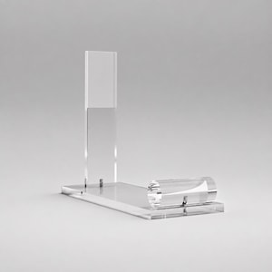 Puede incluir: Un expositor de acrílico transparente que cuenta con una base rectangular, un panel trasero vertical y una pequeña pieza de soporte cilíndrica horizontal unida a la parte frontal. La estructura es transparente, lisa y consta de varias piezas.