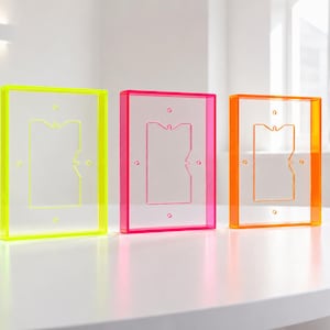 May include: Three rectangular light switch covers made of transparent acrylic. Each cover features a neon-colored border in yellow, pink, or orange, with a central rectangular cutout and four small circular screw holes for installation.