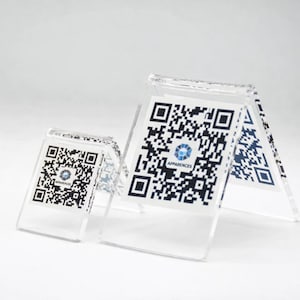 Peut inclure: Présentoirs en acrylique transparent avec codes QR imprimés. Les présentoirs sont de différentes tailles et comportent le mot "APPARENCES" et un logo. Les codes QR sont en noir et blanc.