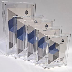Può includere: Un set di cornici per foto in acrilico trasparente di varie dimensioni. Ogni cornice mostra un design geometrico con forme blu e grigie. Le cornici sono disposte in ordine decrescente, con la cornice più grande sul retro. La cornice più piccola misura 12x17cm.