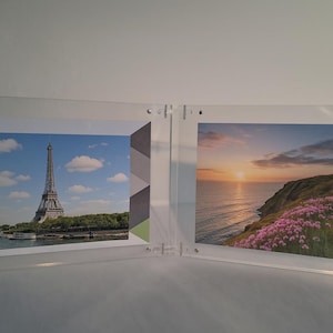 Peut inclure: Cadre photo double face en acrylique transparent. Une face présente la Tour Eiffel, l'autre un coucher de soleil côtier. Le cadre est maintenu par de petites vis argentées. Les photos sont en format paysage.