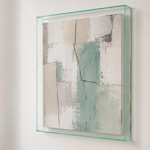 Peut inclure: Une peinture abstraite carrée présentant une composition texturée de blocs rectangulaires blancs, beiges et vert sauge. L'œuvre est encadrée dans une boîte en verre transparent, avec de fines lignes verticales sombres et irrégulières.