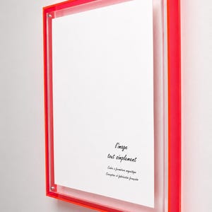 Pode incluir: Uma moldura retangular com uma borda de acrílico laranja neon vibrante e um painel frontal de acrílico transparente. A moldura possui um sistema de fecho magnético e contém uma inserção branca com o texto preto l'image tout simplement.