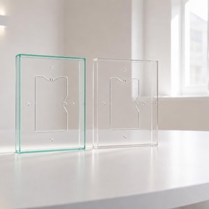 Pode incluir: Dois quadros retangulares de acrílico transparente em posição vertical. O quadro da esquerda tem um tom verde subtil nas bordas, enquanto o da direita é totalmente transparente. Ambos apresentam um recorte retangular central com furos.