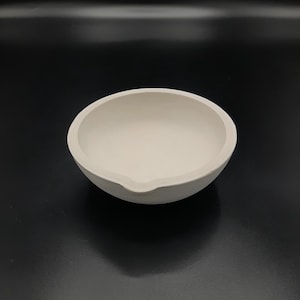 Op de afbeelding: Een witte keramische smeltkroes, een kleine komvormige container die wordt gebruikt voor het smelten van metalen.