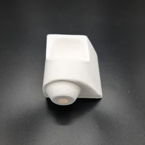 May include: White ceramic crucible with a rounded bottom and a rectangular opening. The crucible is designed for melting and casting metal.
