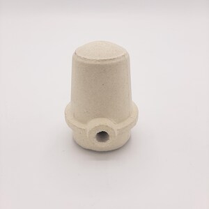 May include: A white ceramic insulator with a hole in the center. The insulator has a rounded top and a textured surface.