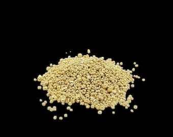 May include: A pile of small, irregularly shaped, golden-colored metal beads against a black background. The beads have a shiny, reflective surface, suggesting they are made of a precious metal like gold.