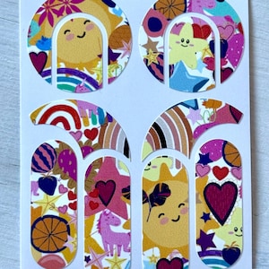 以下が含まれることがあります： さまざまなデザインのカラフルなネイルアートステッカーのシート。ステッカーは、ピンク、黄色、青、オレンジの色合いで、笑顔の太陽、ハート、虹、星、ユニコーンを特徴としています。ステッカーは白い背景にあります。