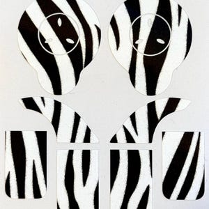 May include: A collection of zebra-striped stickers in various shapes. The set includes two oval shapes with a circular design, two curved shapes, and three rectangular shapes. The stickers feature a black and white pattern.