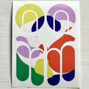 Puede incluir: Una hoja de pegatinas coloridas con diseños abstractos. Cada pegatina presenta una parte superior redondeada con un arco curvo y dos rectángulos verticales debajo. Los diseños incluyen formas amarillas, moradas, verdes, rojas y azules.