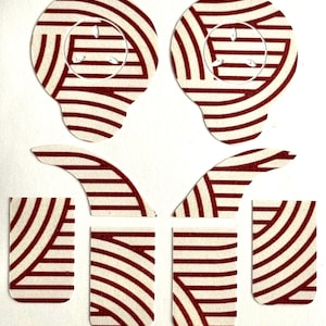 Puede incluir: Un conjunto de pegatinas troqueladas de color crema con un patrón repetitivo de líneas rojas curvas. El conjunto incluye dos piezas grandes en forma de oreja, dos formas curvas en forma de ala y cuatro piezas rectangulares. Las pegatinas están dispuestas sobre un fondo blanco.