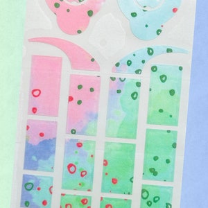 Op de afbeelding: Een vel kleurrijke stickers met een aquarelontwerp. De stickers hebben roze, blauwe en groene tinten met rode en groene stippen. De vormen omvatten cirkels, rechthoeken en gebogen elementen.