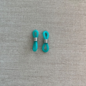 Op de afbeelding: Twee turquoise siliconen brilkettingverbinders met een flexibel lusontwerp en een zilverkleurige metalen spiraalveer die verschuift om de brilpootjes vast te zetten, wat zorgt voor een functionele bevestiging voor brilaccessoires.