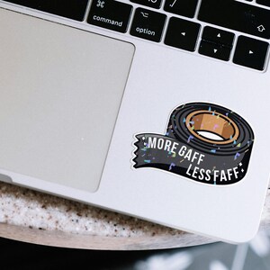 K&ouml;nnte beinhalten: Ein Aufkleber mit einer Rolle schwarzem Gaffaband mit braunem Kern. Der Aufkleber hat den wei&szlig;en Text "MORE GAFF LESS FAFF". Der Aufkleber befindet sich auf einem Laptop.