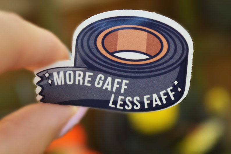 K&ouml;nnte beinhalten: Ein Aufkleber mit einer Rolle dunkelblauem Klebeband mit brauner Mitte. Der Aufkleber tr&auml;gt den wei&szlig;en Text "MORE GAFF LESS FAFF". Der Aufkleber wird in einer Hand gehalten.