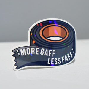 K&ouml;nnte beinhalten: Aufkleber mit einem Klebebandrollen-Design in Dunkelblau und Braun. Der Text "MORE GAFF LESS FAFF" ist wei&szlig;. Der Aufkleber hat einen holografischen Effekt.