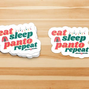 Puede incluir: Dos pegatinas blancas con el texto "eat sleep panto repeat" en rojo, verde y blanco. La palabra "eat" está en rojo, "sleep" está en verde y "panto" está en rojo. Un pequeño gráfico de suéter está entre "eat" y "sleep".