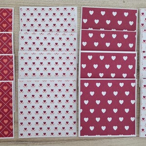 Può includere: Una collezione di cartoline rettangolari con tre motivi distinti: uno sfondo rosso scuro con una griglia di cuori rosa chiaro, uno sfondo bianco con piccoli motivi a cuore rosso scuro e uno sfondo rosso scuro con motivi a cuore bianchi.