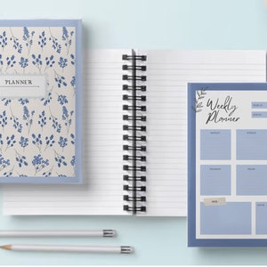 May include: Two spiral bound notebooks with blue covers. The front cover of the left notebook has a floral pattern with blue flowers and leaves on a white background. The front cover of the right notebook has a blue background with the text "Weekly Planner" in black.