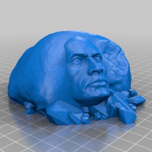 May include: A blue 3D printed sculpture of a face emerging from a rock. The face is detailed with a furrowed brow, a strong jawline, and a serious expression.