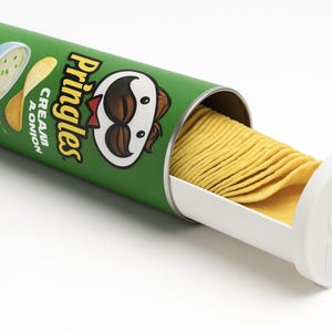 Puede incluir: Una lata verde de Pringles con una bandeja extraíble blanca llena de patatas fritas onduladas. La lata presenta el logotipo de Pringles y las palabras "Cream & Onion". La bandeja tiene la cara de la mascota de Pringles.