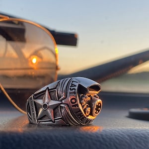 Puede incluir: Un anillo de plata con una estrella y las palabras "Last of the V8" grabadas en él. El anillo presenta un diseño de motor detallado.