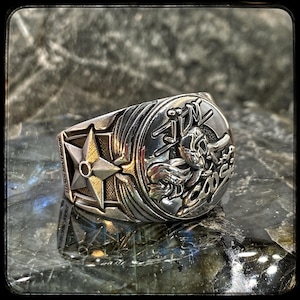 Pode incluir: Um anel de prata com uma estrela e um design detalhado com um personagem de desenho animado com o texto "JIN" e "BOSS".