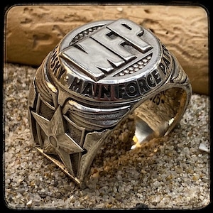 May include: A silver ring with a star and wings design. The ring has the words "MFP Main Force Patrol" engraved on the top.